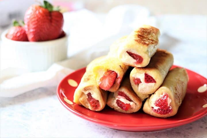 french toast roll ups on top of a red plate next to strawberries. 