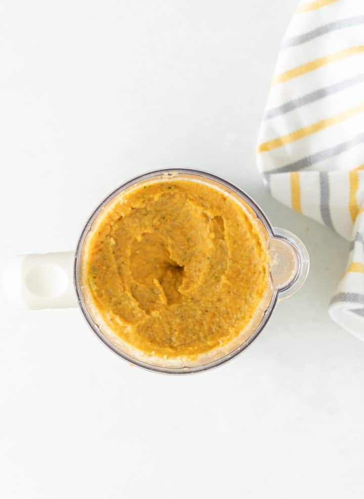 Blender with orange blended veggie mixture, yellow and gray kitchen towel 