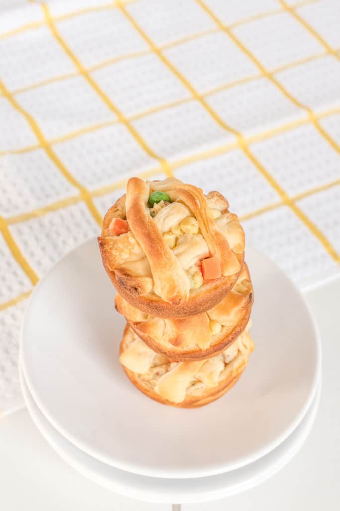 Stacked Chicken pot pies on a white plate with a yellow checkered white kitchen towel