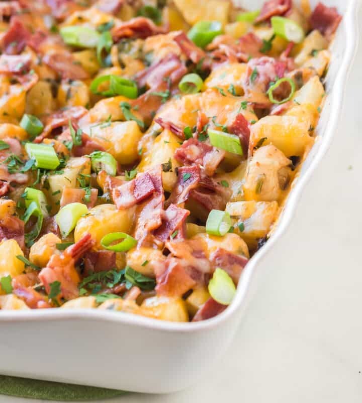 Cooked dish of baked chicken and potatoes with bacon and onion on top
