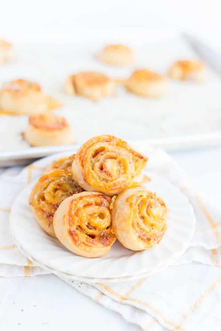 cheesy pinwheels on a white plate with baking sheet in the back