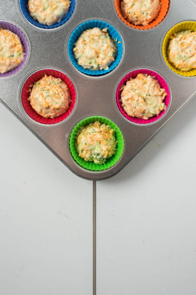 Muffin tin with batter ¾ filled inside colorful silicone liners