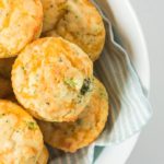 Close up of several broccoli cheese muffins in a white bowl over a teal and white stripe dish towel