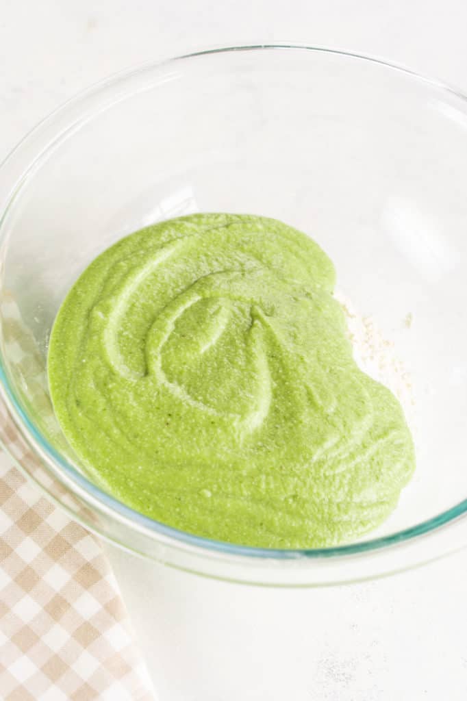Bowl of green mixture and flour under, gingham kitchen towel 