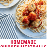 Plate of spaghetti with homemade chicken meatballs and spaghetti with red sauce on a plate. Another plate with partial view of pasta and meatball and side napkin that is striped gray and white