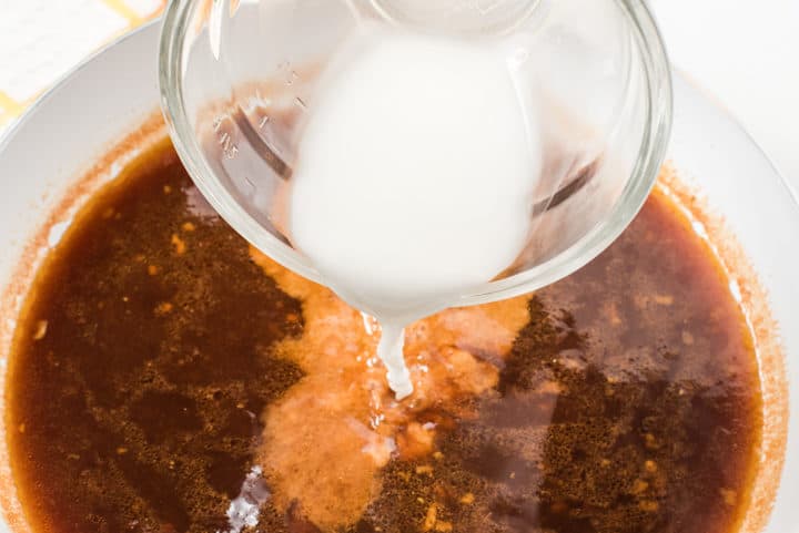 Clear bowl with cornstarch and water mixture being poured into soy sauce mixture 