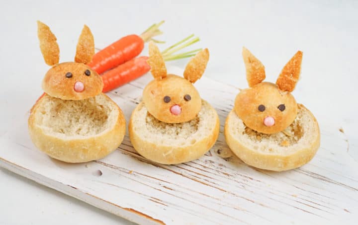 Empty bunny shaped bread bowls with carrots in the background on top of white wooden board
