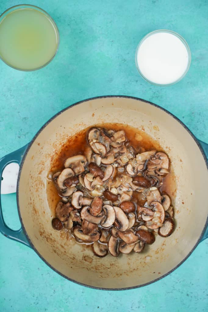 Large pot of mushrooms with broth and madeira wine on teal background