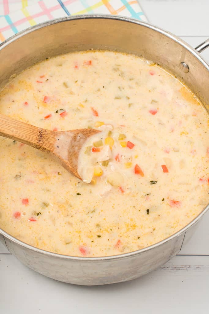Close up of cooked chowder in a pot, with a wooden spoon