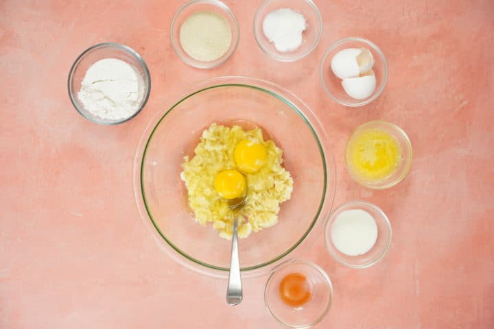Bowls of ingredients with eggs in larger bowl and mashed banana 