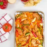 Sheet pan of cooked chicken fajitas with tomato on the side