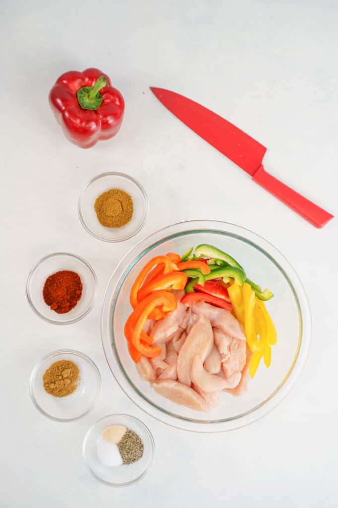 Bowl of chicken bell peppers and ingredients in small bowls 