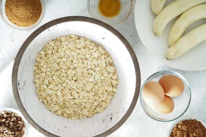 Bowls of ingredients including oats, eggs, bananas, coconut sugar, vanilla extract and bananas