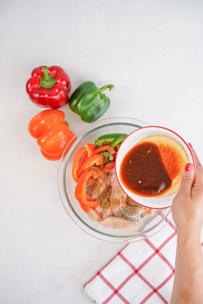 hand pouring marinade over chicken and vegetables in a bowl