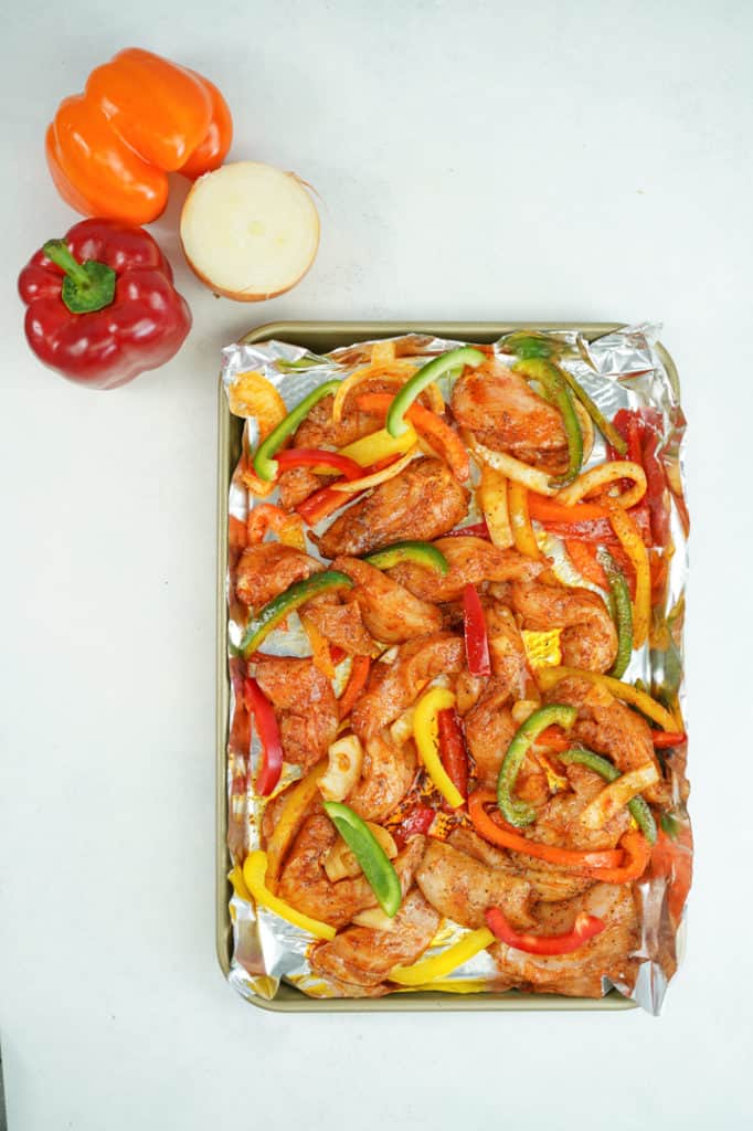 Sheet pan lined with foil with raw chicken and marinated vegetables with onion and bell peppers on the side