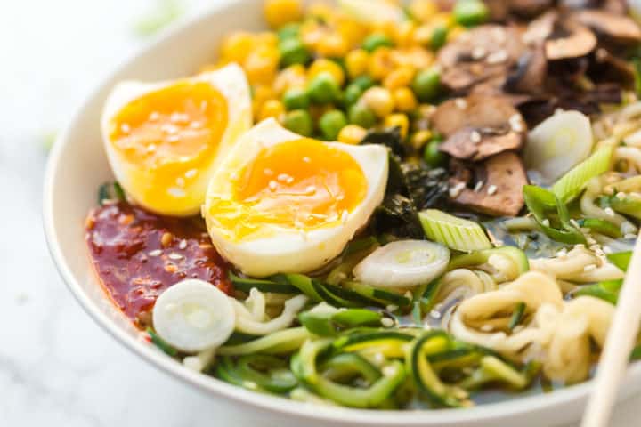 close up of ramen soup with eggs, corn peas, zucchini noodles and regular noodles.