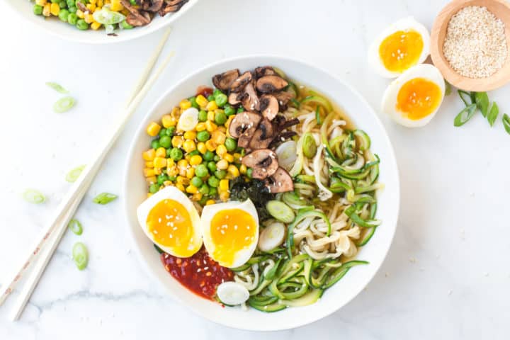 Bowl of ramen noodles with zucchini spirals, vegetables, mushrooms, hard boiled eggs and sambal