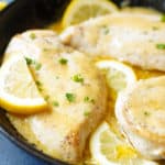 Close up of chicken glazed with lemon butter and fresh parsley as ganish, also sliced lemons