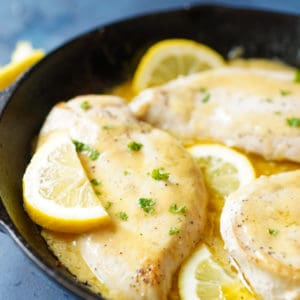 Close up of lemon butter chicken in a cast iron pan with sliced lemons on top and fresh parsley