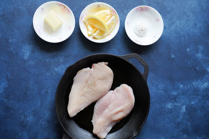 Raw chicken in cast iron pan next to ingredients