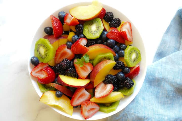 bowl of fruit including strawberry, kiwi, peaches, blueberries, and blackberries