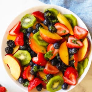 bowl of fruit including kiwi, strawberris, peahes, blueberries ad blackberries