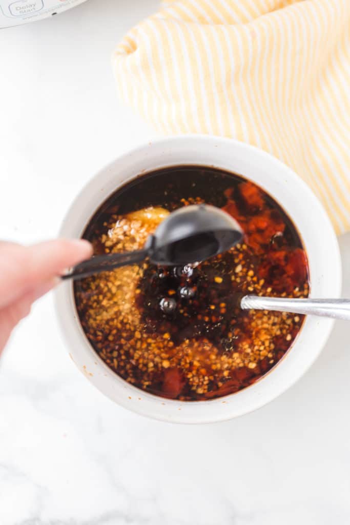 Bowl of soy sauce with spices and a spoon adding sesame oil 