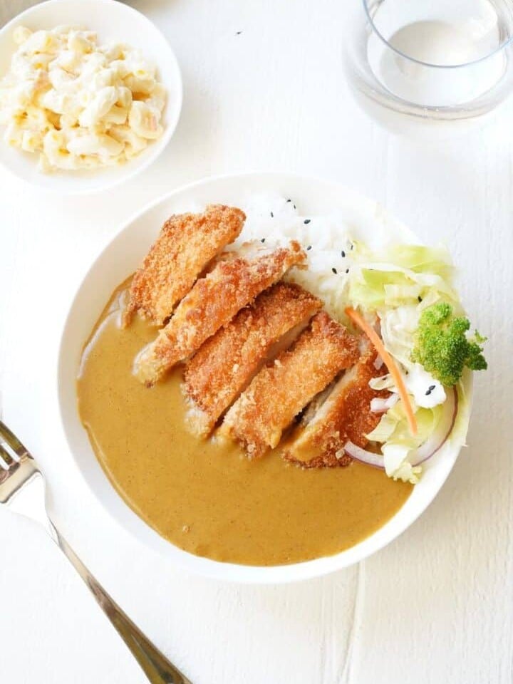 Bowl of curry with breaded chicken in white bowl with vegetables and macaroni on the side