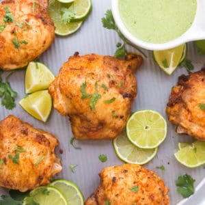 Close of up of roasted chicken thighs with lime around and green sauce