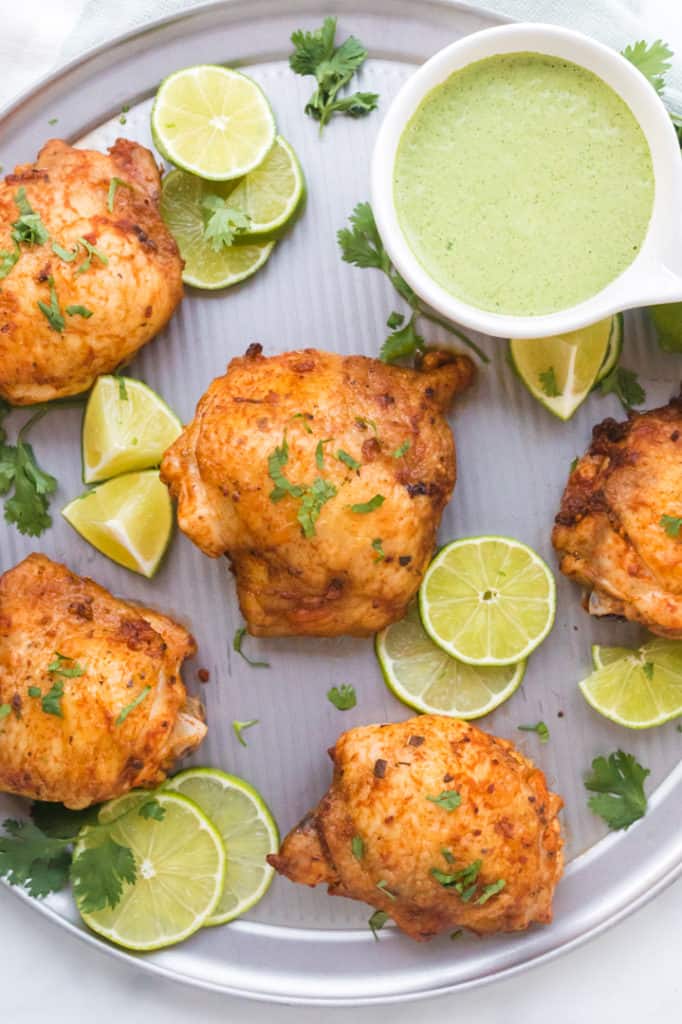 Close of up of roasted chicken thighs with lime around and green sauce 