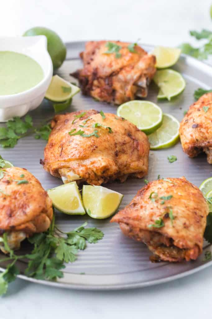 Close up of chicken thighs with lime and green sauce on the side
