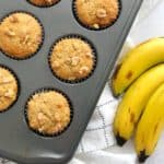 Over the top shot of muffins in muffin tin with bananas on the side