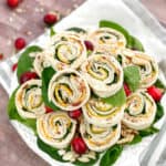 Stack of cranberry turkey pinwheels on a plate with cranberries around.