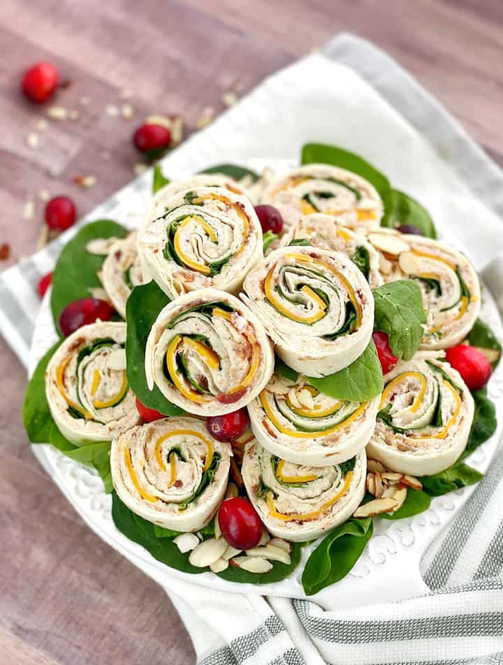 Stack of cranberry turkey pinwheels on a plate with cranberries around.