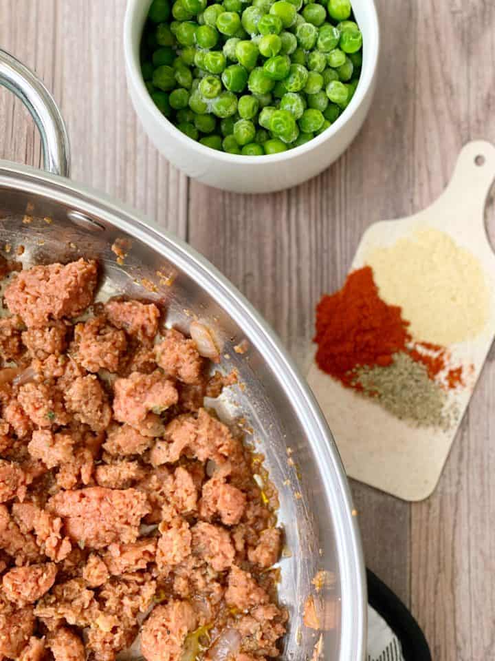 pan with ground meat and seasonings, next to a small bowl of peas