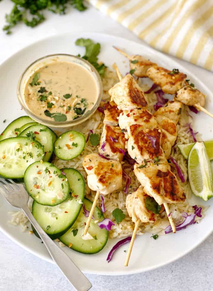 Chicken satay on a plate with cucumbers