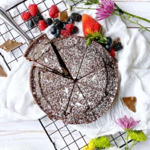 chocolate cake on a plate with berries and flowers around it