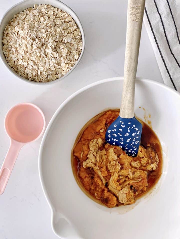 Bowl of pumpkin puree and oats next to a pink measuring spoon for pumpkin oatmeal bars 