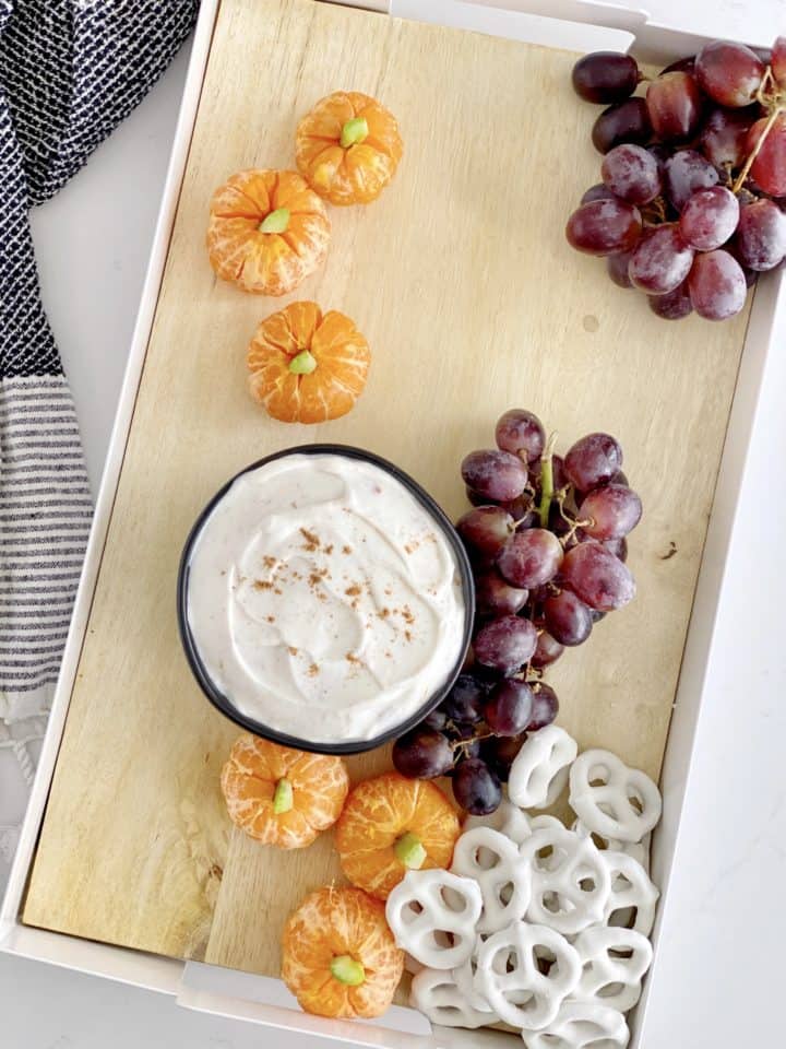snack board with tangerines, grapes, dip and pretzels 