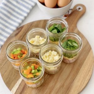mason jars of toppings for egg scramble on a wood board