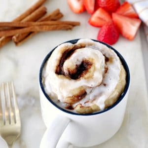 cinnamon roll in a mug with cinnamon sticks in the background