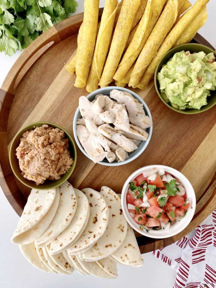 board with taquitos, bowls of guacamole, beans, and salsa 