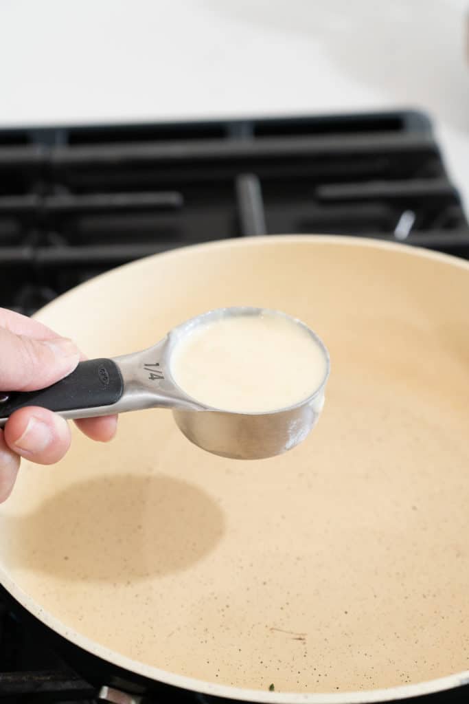pan with hand holding a measuring cup over a skillet 