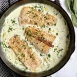 pan with cream sauce and salmon filets in a pan