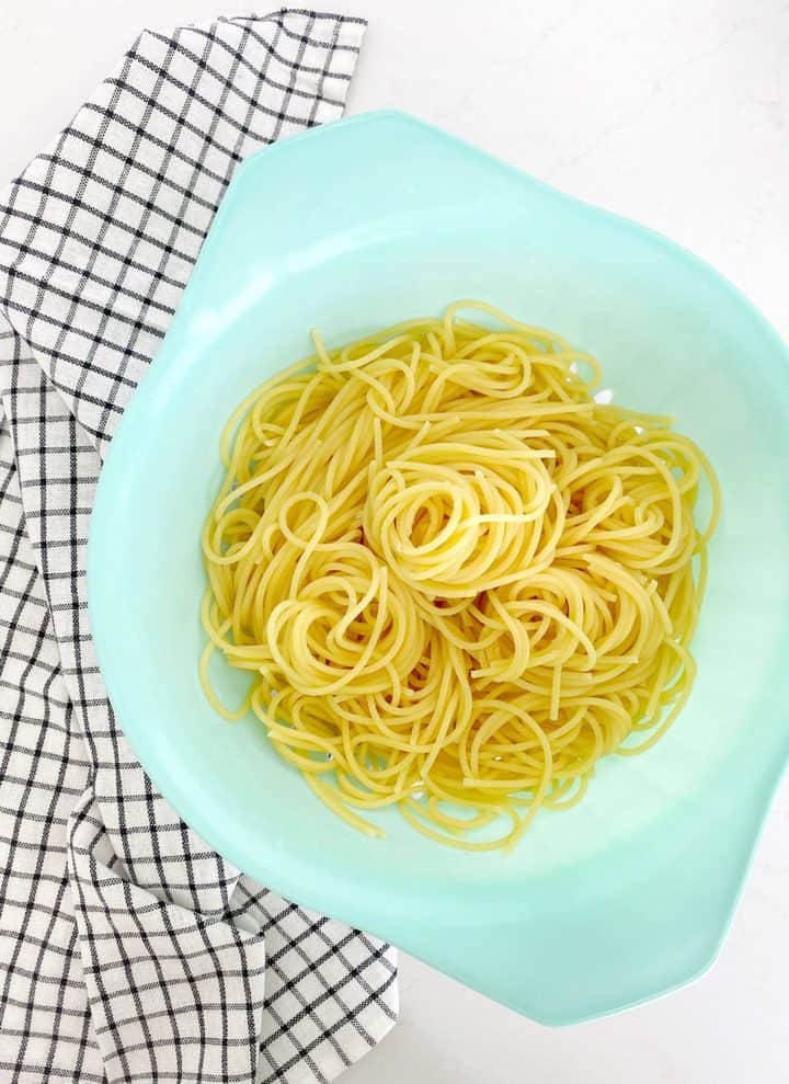 teal colander with cooked spaghetti noodles 