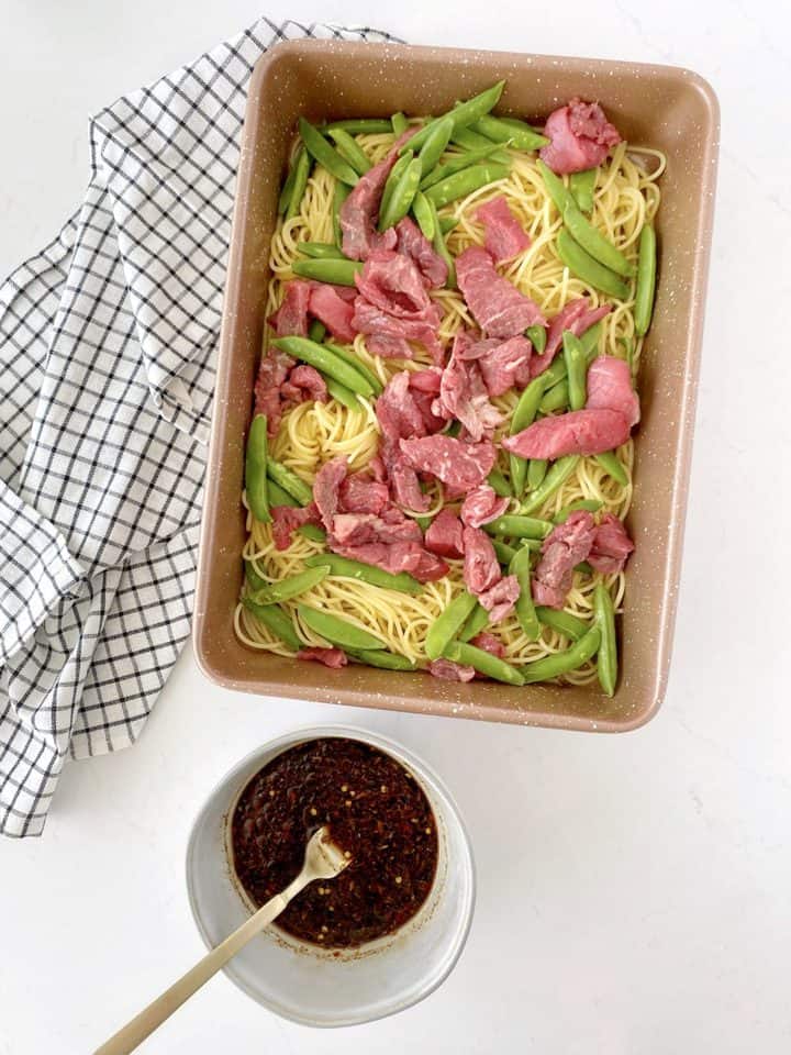 pan with noodles, beef and snowpeas next to a sauce 
