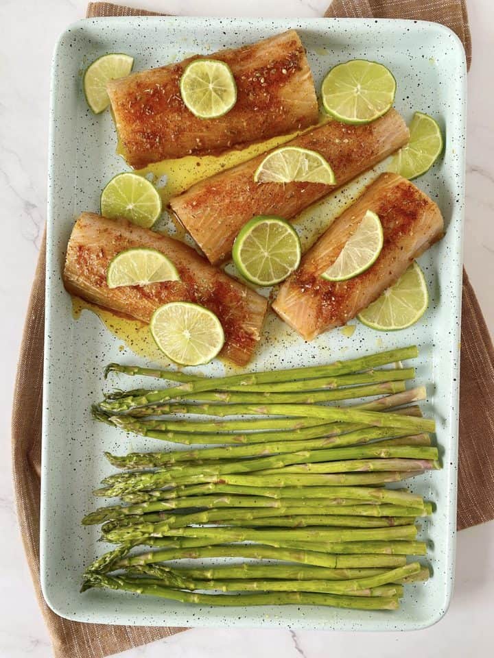 baking sheet with asparagus with fish and lime on top 