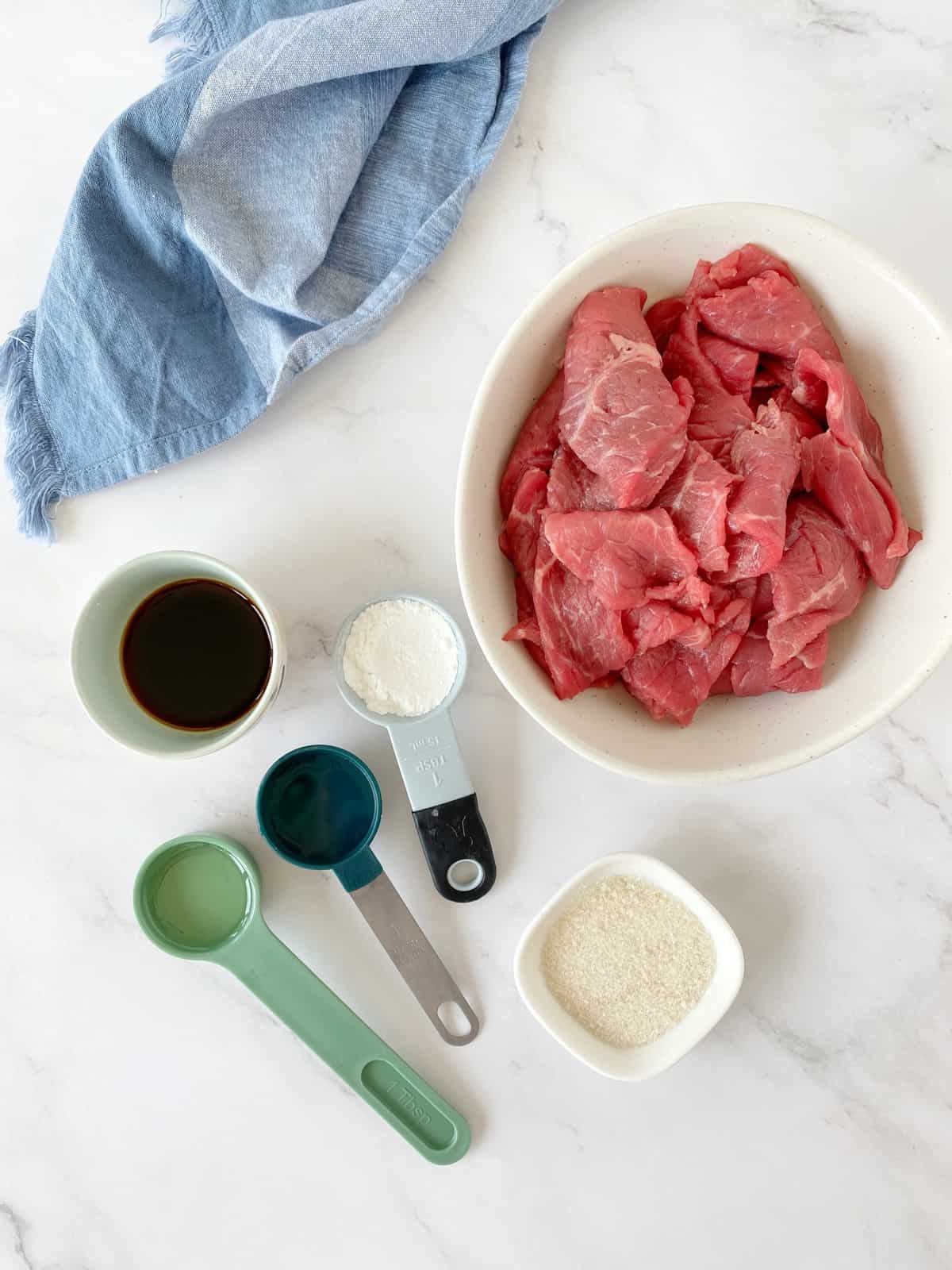 bowl of beef and measuring spoons of filled ingredients like soy sauce and vinegar 