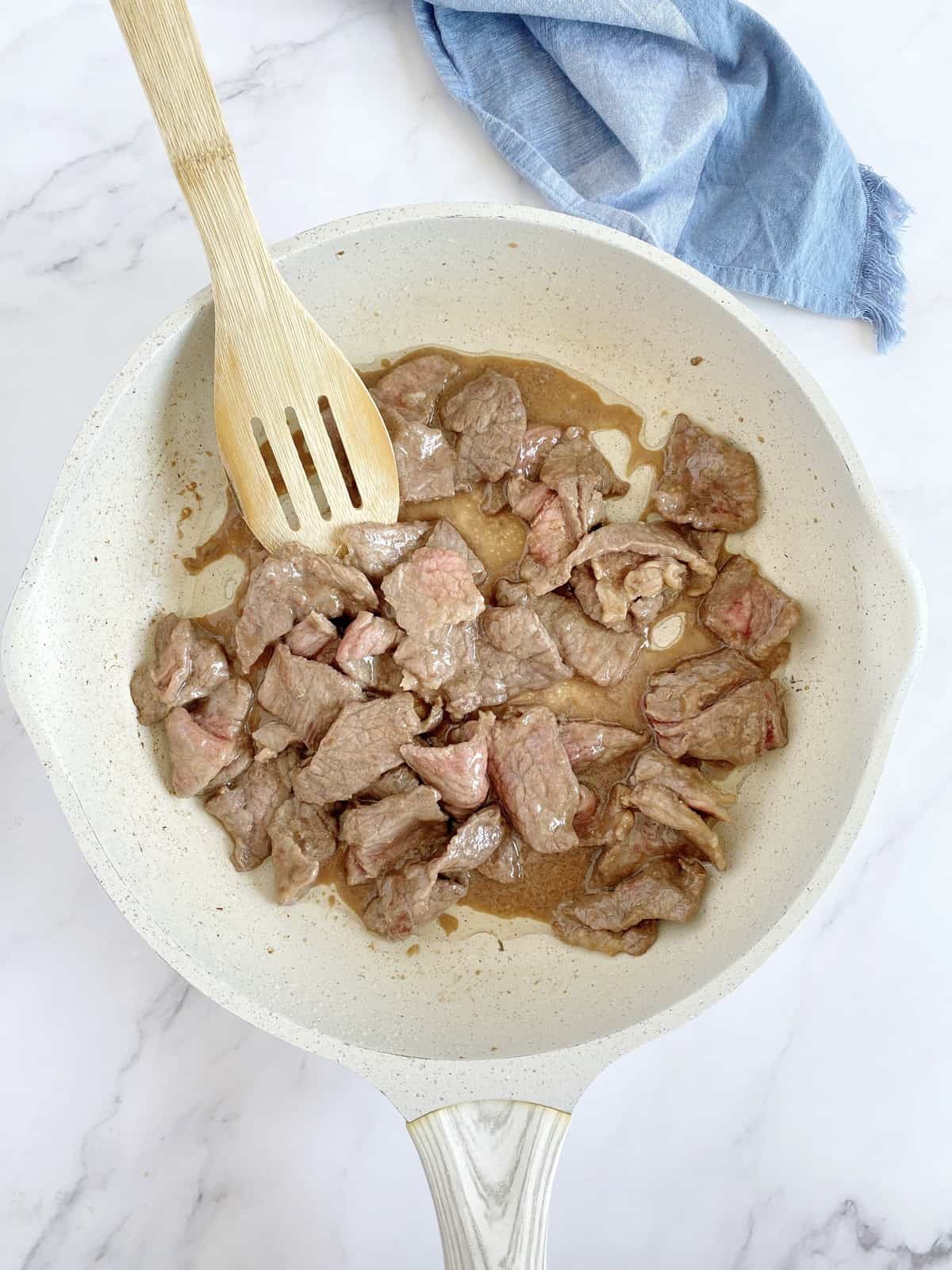 cooked beef in a pan next to wooden spoon 