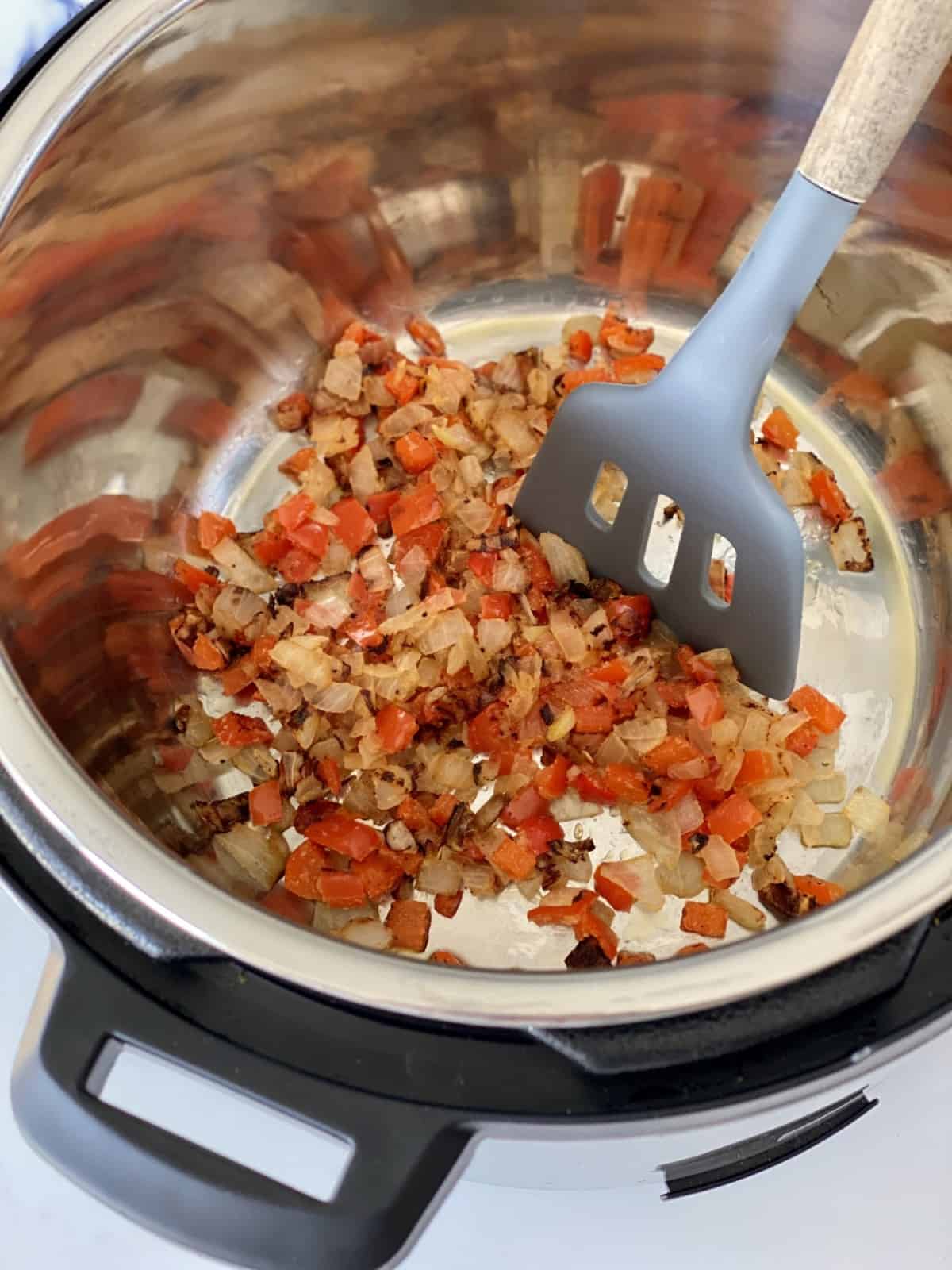 close up of onions and tomatoes in a pressure cooker with a spatula 